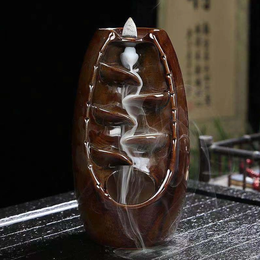 Reddish-brown backflow incense burner with active smoke cascade flowing down spiral channel, three-quarter view