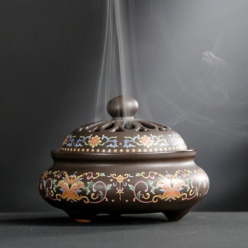 Dark brown ceramic incense burner with colorful floral scroll patterns, three-footed base, rising incense smoke visible