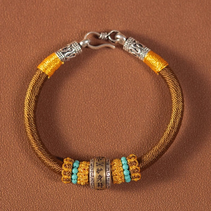 Brown Buddhist King Kong Knot braided bracelet with silver clasp and engraved charm with turquoise accents on table