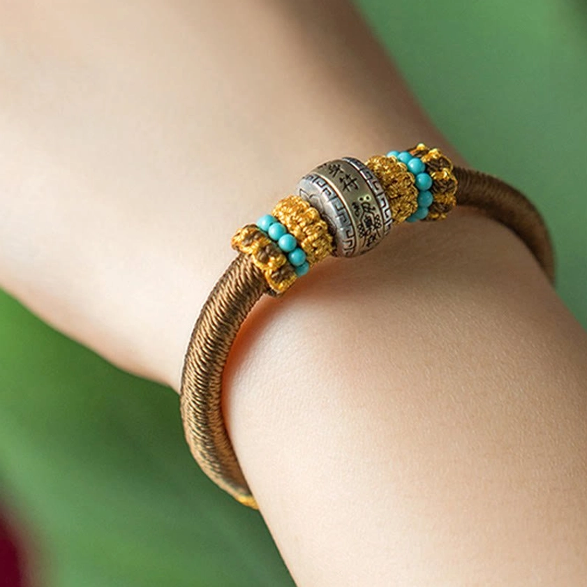 Brown Buddhist lucky bracelet worn on wrist with foliage background showing central metal bead and beaded decorations clearly