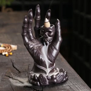 Dark brown ceramic skull hand backflow incense burner with flowing smoke on wooden surface
