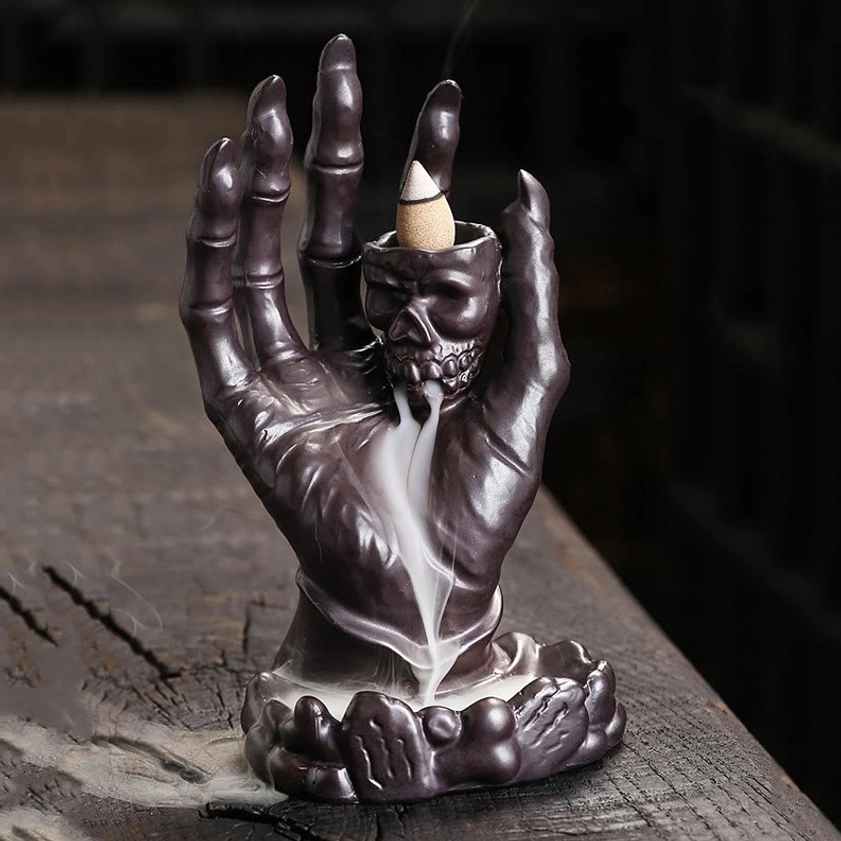 Brown glazed ceramic skull hand incense burner showing smoke trail effect from backflow design