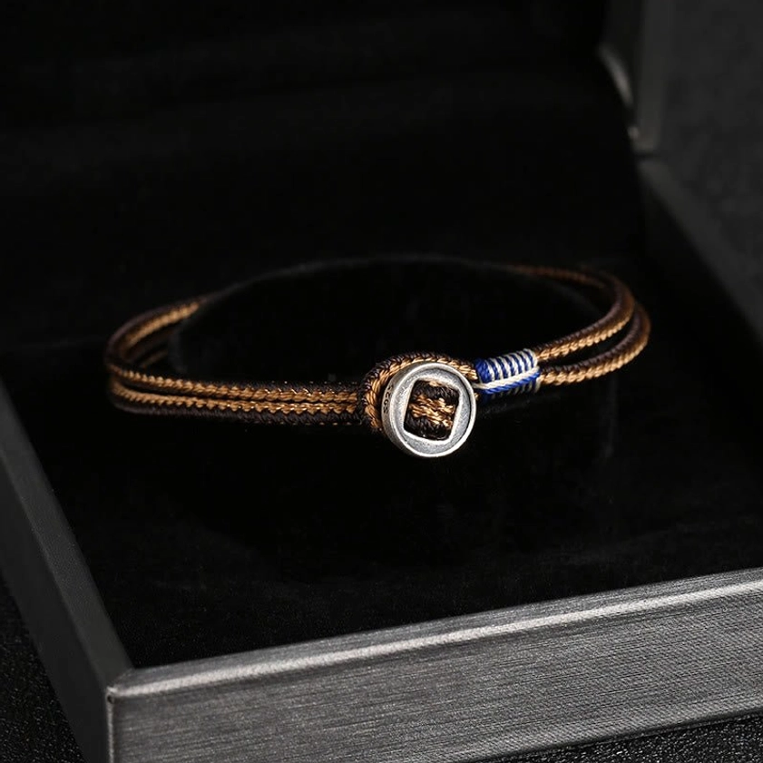 Solid brown woven Buddhist bracelet with round metal decorative buckle, stored in open jewelry box display