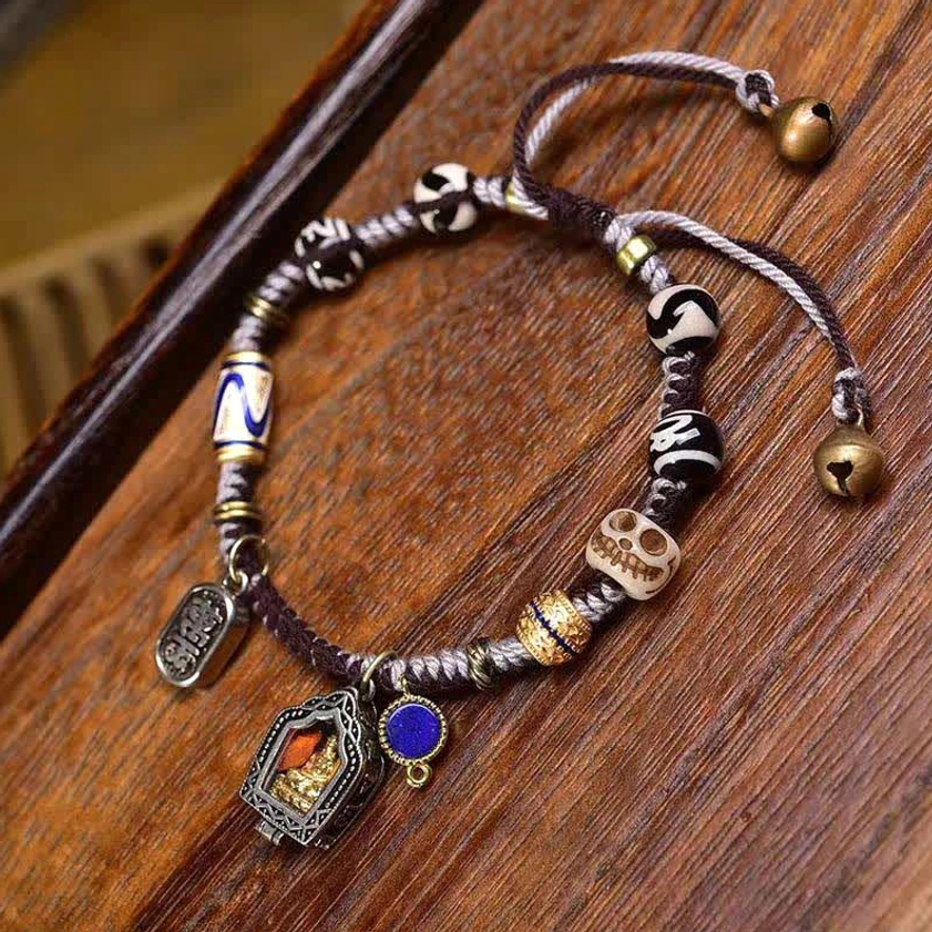 Close-up detail of Buddhist braided bracelet showing Dzi beads, small bell charm, and decorative copper components