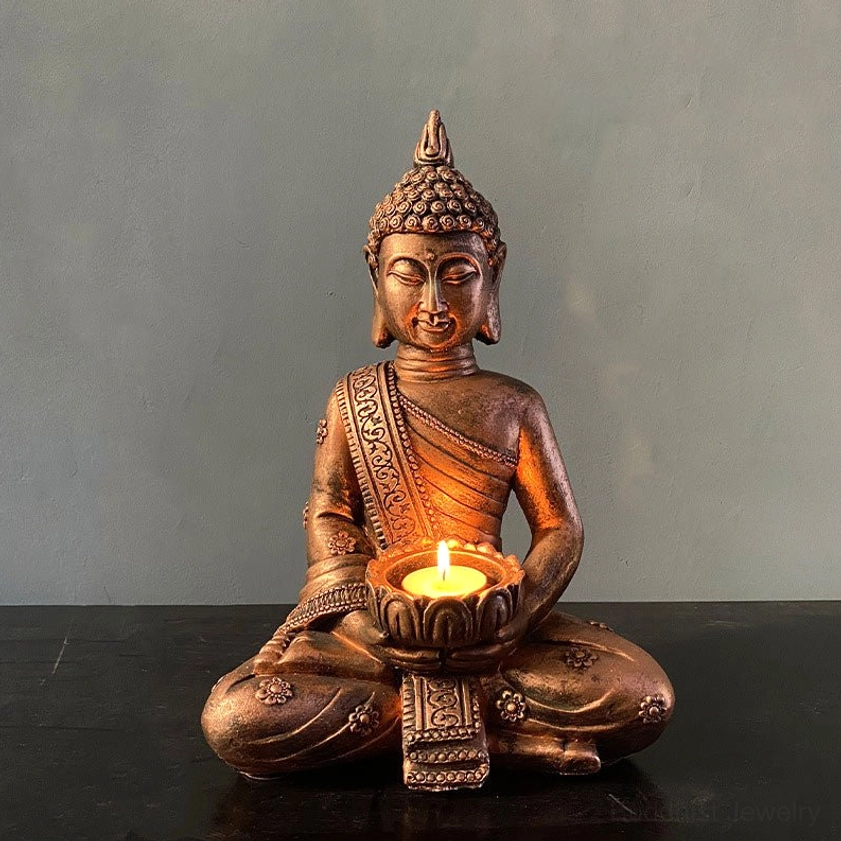 Antique bronze Buddha candlestick holder with lit tealight candle, front view showing intricate carved robe details and serene face
