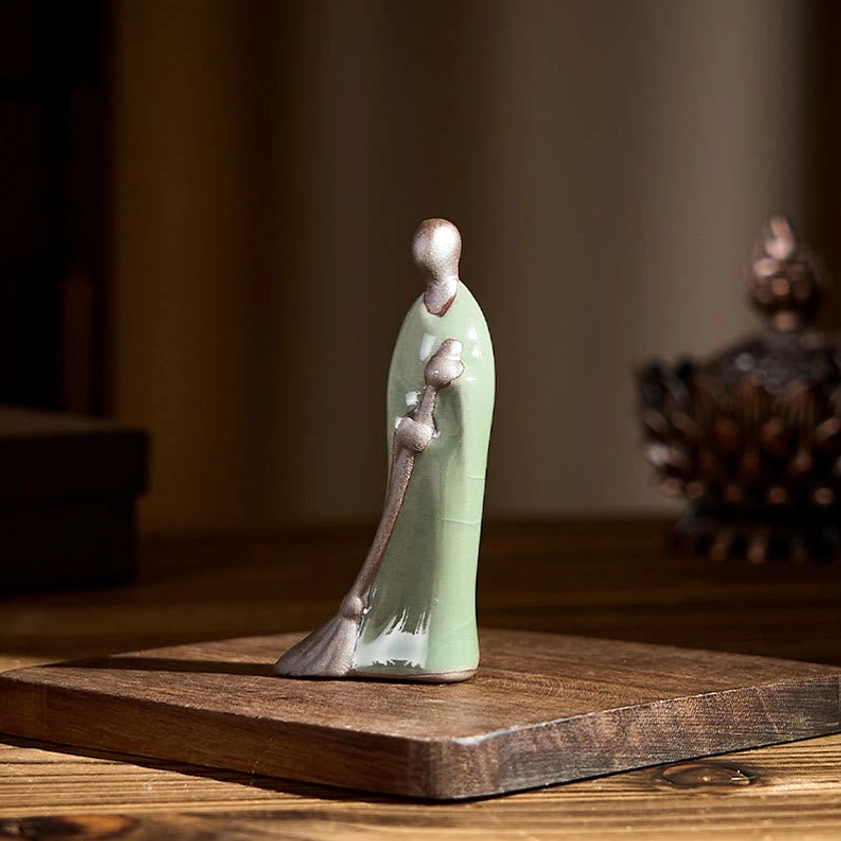 Faceless sweeping monk Buddha ceramic decoration right side profile with bronze accents and celadon glaze on wooden surface