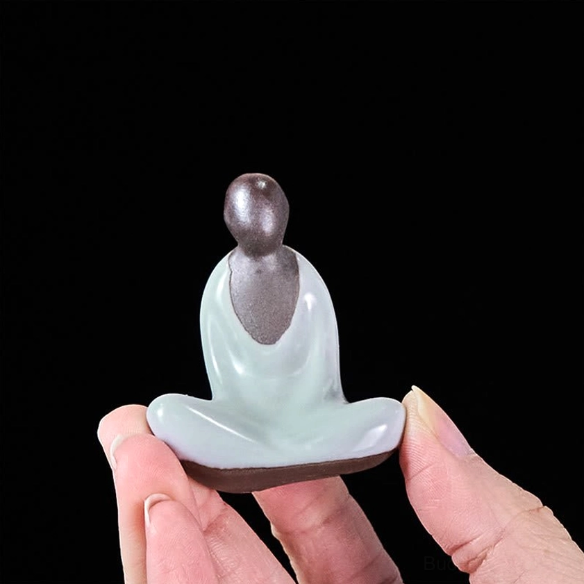 Ceramic Buddha meditation statue held between fingertips showing miniature portable size