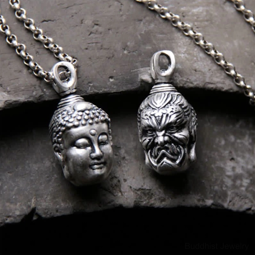 Double-faced Buddha and demon silver pendants on chain, top-down shot showing detailed carving on rough stone surface