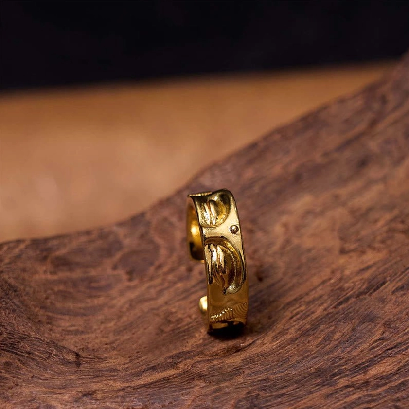Buddha meditation ring in side standing position on natural wooden tabletop showing embossed Buddha face and polished golden finish