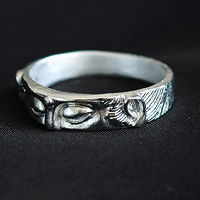 Angled side perspective of sterling silver Buddhist eyes ring displaying matte finish and fine carved patterns on woven fabric