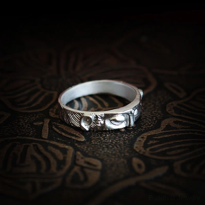 Top-down close-up of Buddha eyes sterling silver ring showing partial embossed eye motifs on dark floral patterned surface