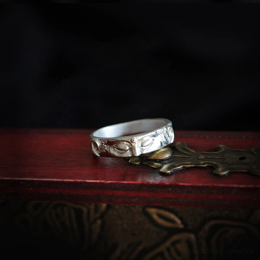 Sterling silver Buddha eyes ring placed on vintage red wooden furniture with carved metal details, low angle view