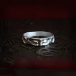 Sterling silver Buddha eyes protection ring with intricate carved engravings on dark vintage patterned surface, frontal flat view