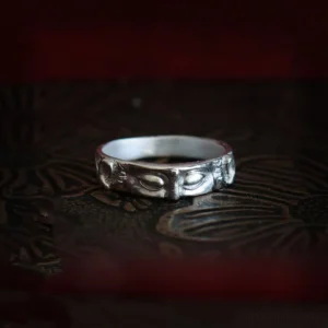 Sterling silver Buddha eyes protection ring with intricate carved engravings on dark vintage patterned surface, frontal flat view