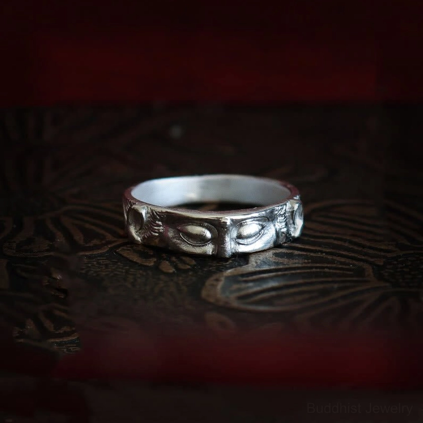 Sterling silver Buddha eyes protection ring with intricate carved engravings on dark vintage patterned surface, frontal flat view