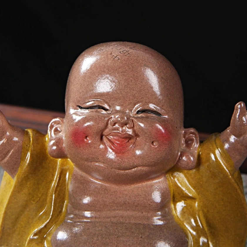 Close-up of laughing Buddha tea pet face on black background showing squinting smiling eyes, red cheek blushes, enlightened expression