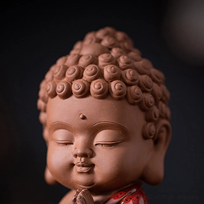 Close-up extreme detail of Sakyamuni Buddha figurine head showing curly hair buns, peaceful expression, third eye mark, and terracotta clay finish