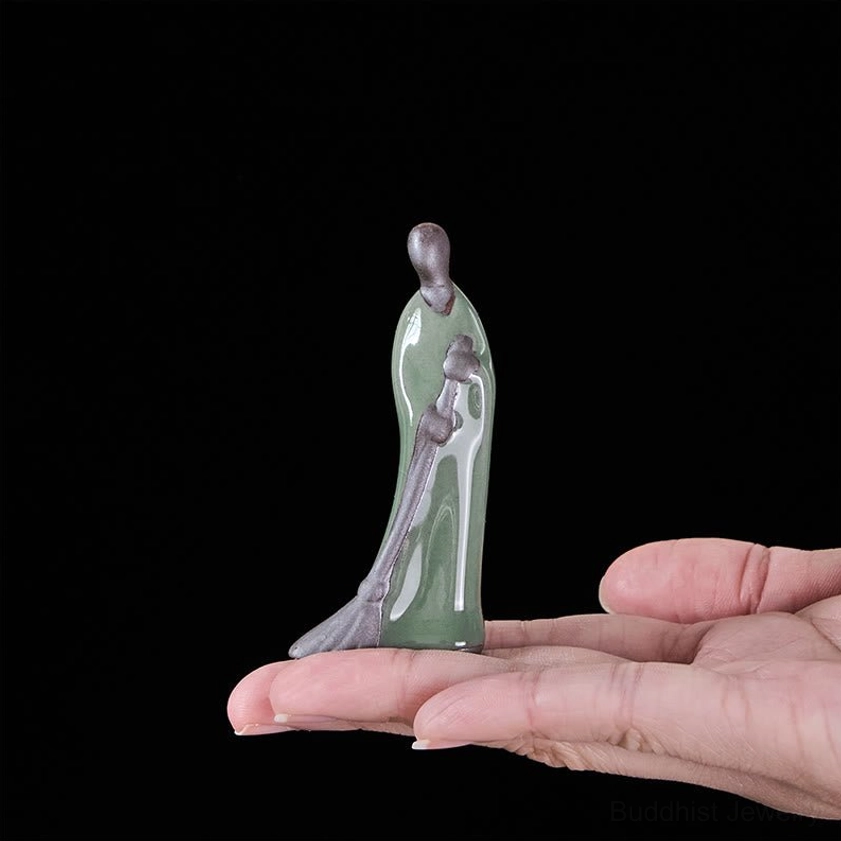 Small Buddha sweeping monk statue held in hand for scale reference showing compact size and celadon green ceramic glaze