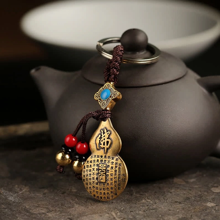 Mahasthamaprapta Buddha gourd keychain with blue stone inlay and engraved Chinese Buddha character, displayed beside clay teapot with red bead tassels and golden bells