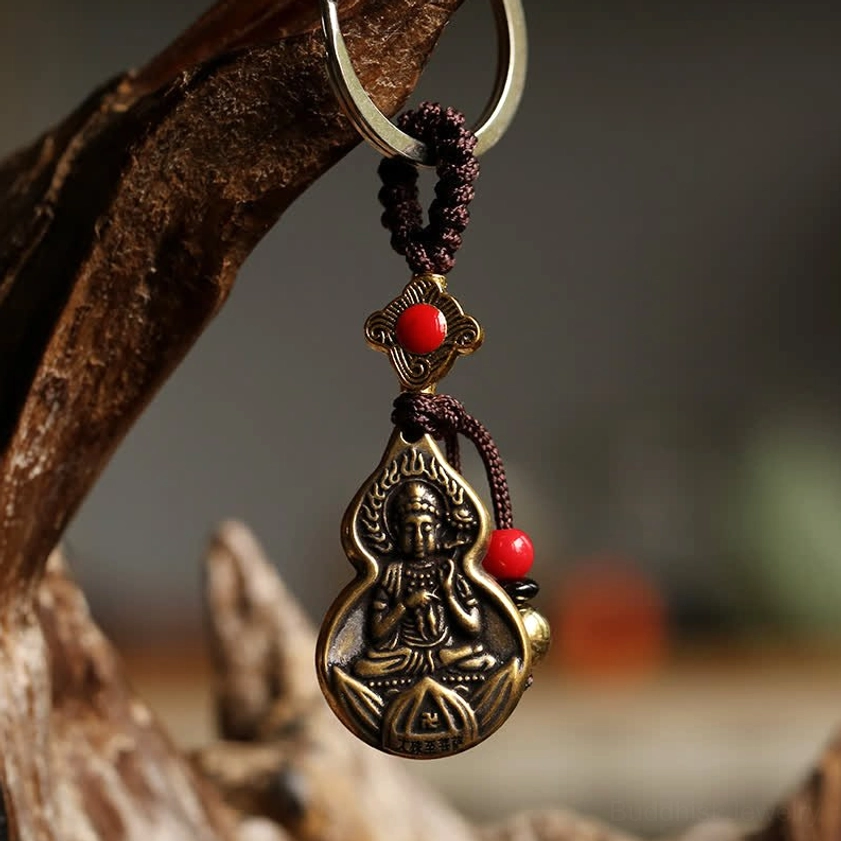 Close-up front view of handcrafted Buddha gourd keychain hanging on wooden branch, featuring antique bronze tone, red and gold bead accents, and carved Buddha motif