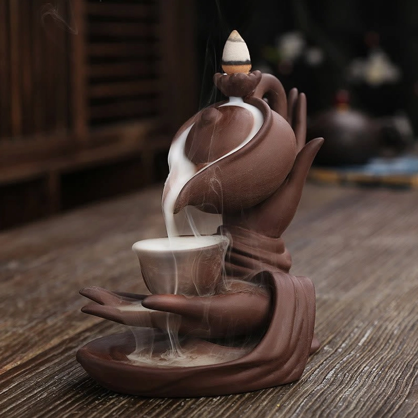 Brown-red Buddha hand ceramic backflow incense burner displaying cascading smoke effect from teapot