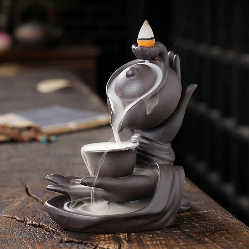 Close perspective of Buddha hand teapot burner with thick white incense smoke pouring into base cup