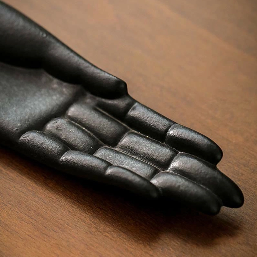 Buddha hand incense burner close-up showing realistic finger texture and matte black ceramic finish