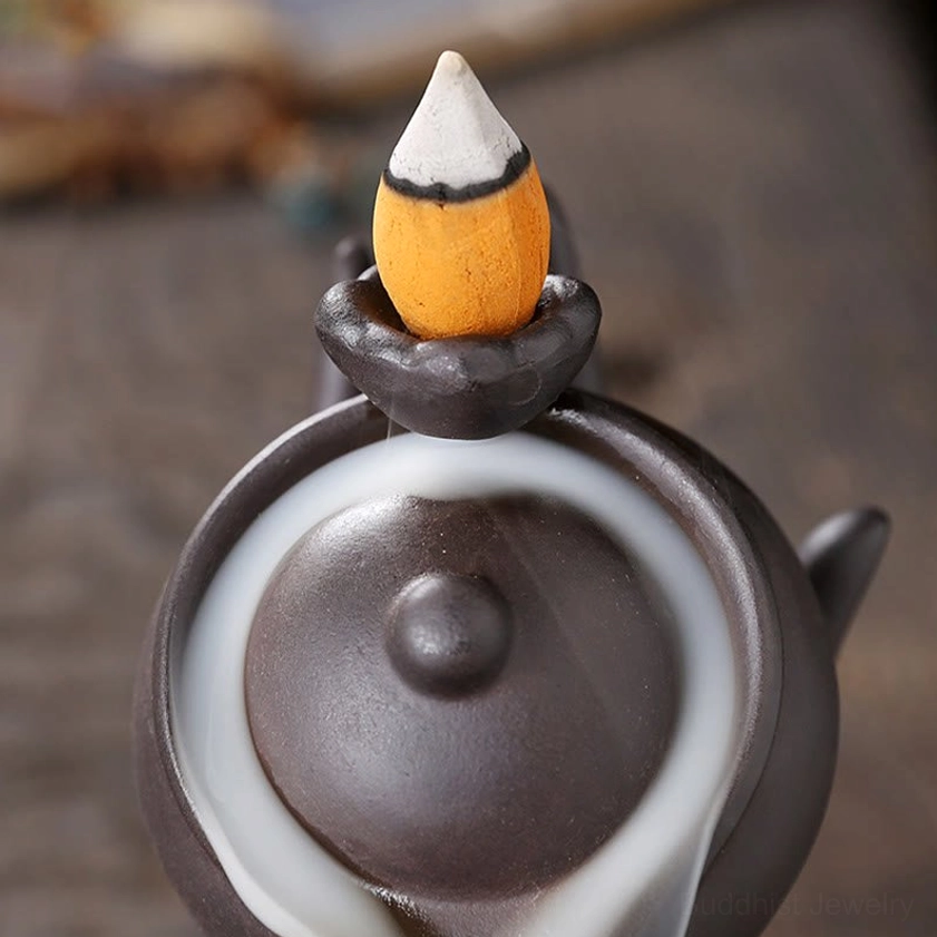 Top view of orange-white backflow incense cone in handmade Buddha hand ceramic burner