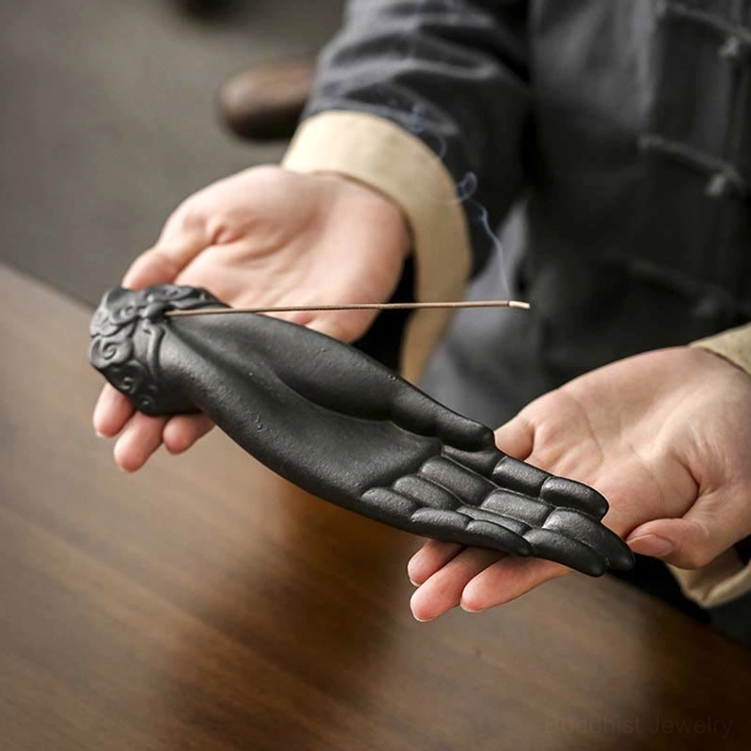 Black ceramic Buddha hand incense holder with realistic palm and finger details, front view showing blessing gesture