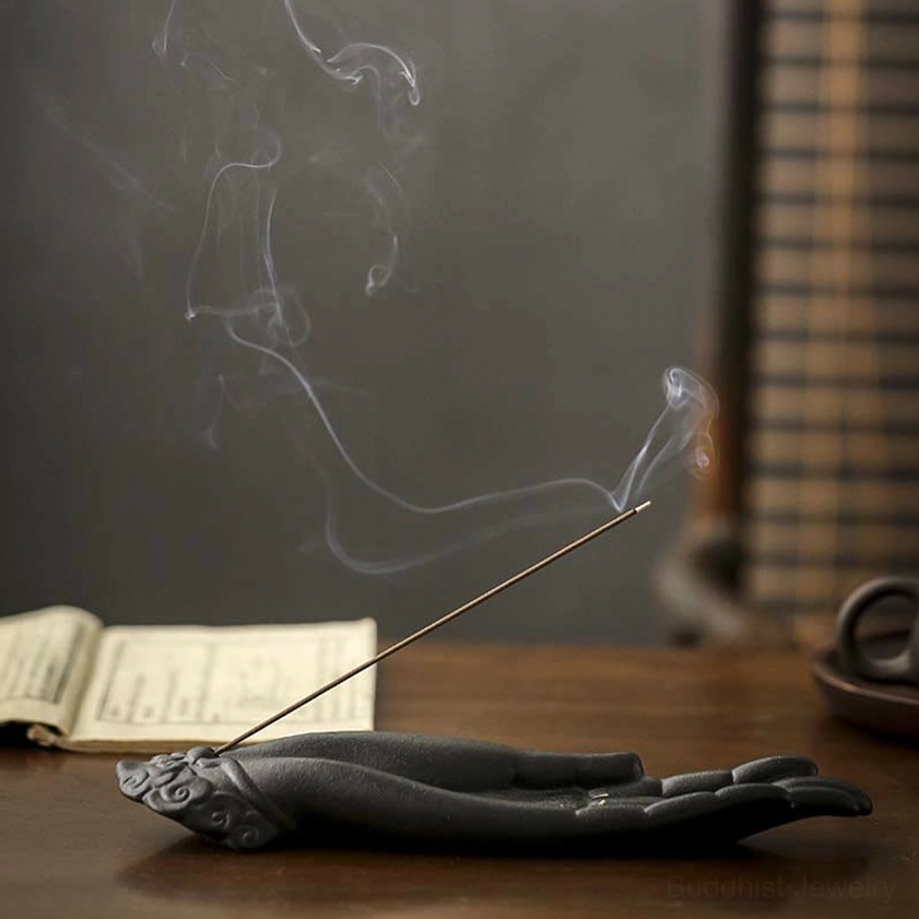 Buddha hand incense burner with rising smoke, matte black ceramic finish on minimalist background