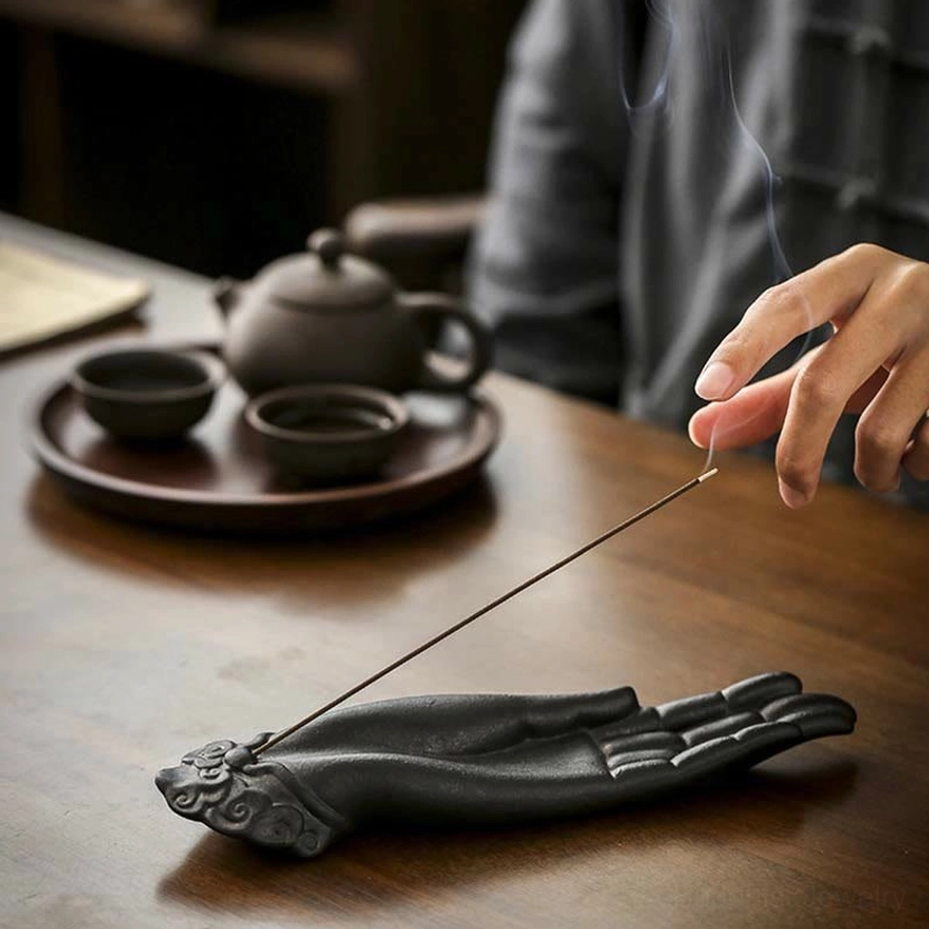 Buddha hand incense holder with smoking incense surrounded by traditional tea setup, eye-level side view