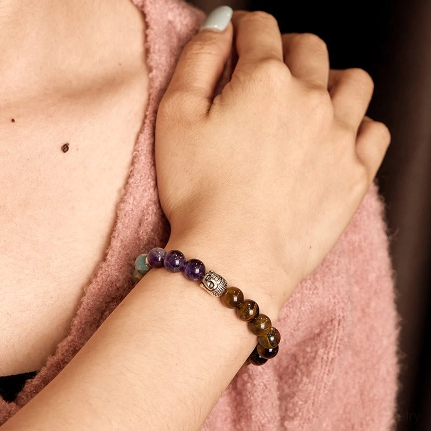 Woman's hand and wrist displaying mixed gemstone Buddha bracelet against pink fabric