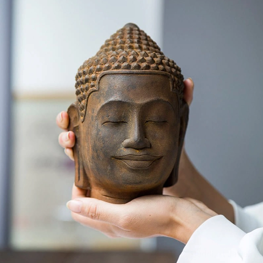 Close-up of Buddha head held in hands showing serene closed-eye expression and weathered rust-brown patina finish