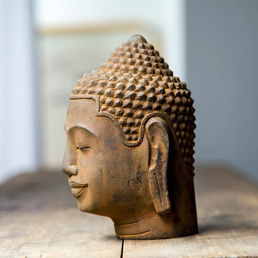 Buddha head statue profile view showing ear, closed eyes, and traditional spiked hair bun, rust-cast resin material
