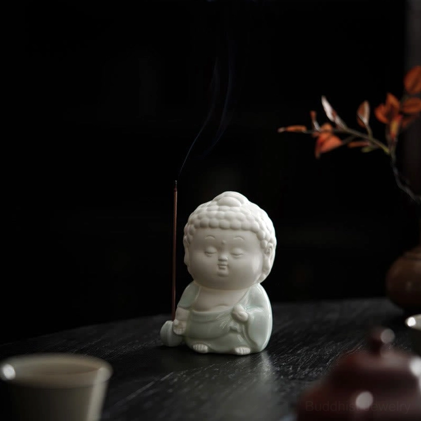 Seated Buddha incense burner with lit incense stick displayed on traditional tea table with celadon robes - three-quarter angle