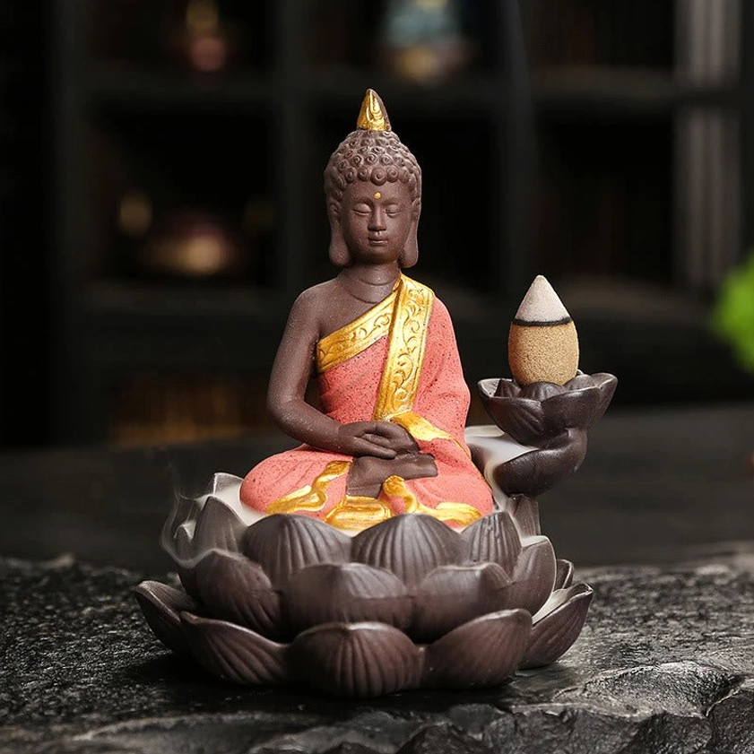 Red Buddha backflow incense burner with gold-trimmed robe detail in meditation pose on dark tabletop setting