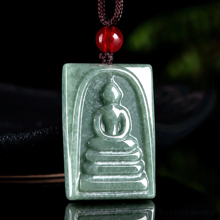 Side-front angle of jade Buddha pendant showing embossed relief carving, dark green jade with red bead attachment