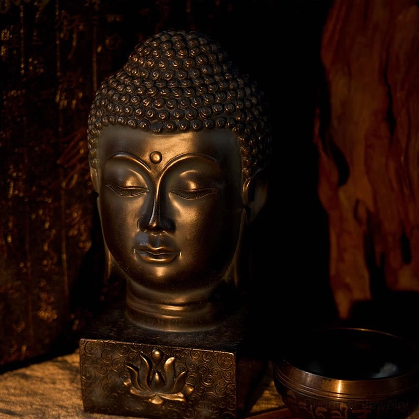 Buddha head decorative statue warm bronze tone with lotus base engraving, dimly lit spiritual tabletop meditation altar setting