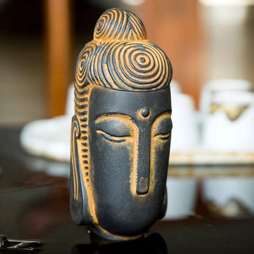 Meditating Buddha head statue with glossy dark finish and rusty yellow decorative details frontal view