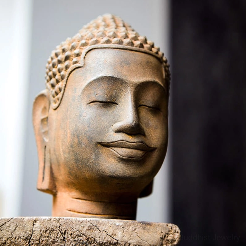 Close-up frontal view of meditating Buddha head statue on wooden stump showing detailed facial features and serene smile