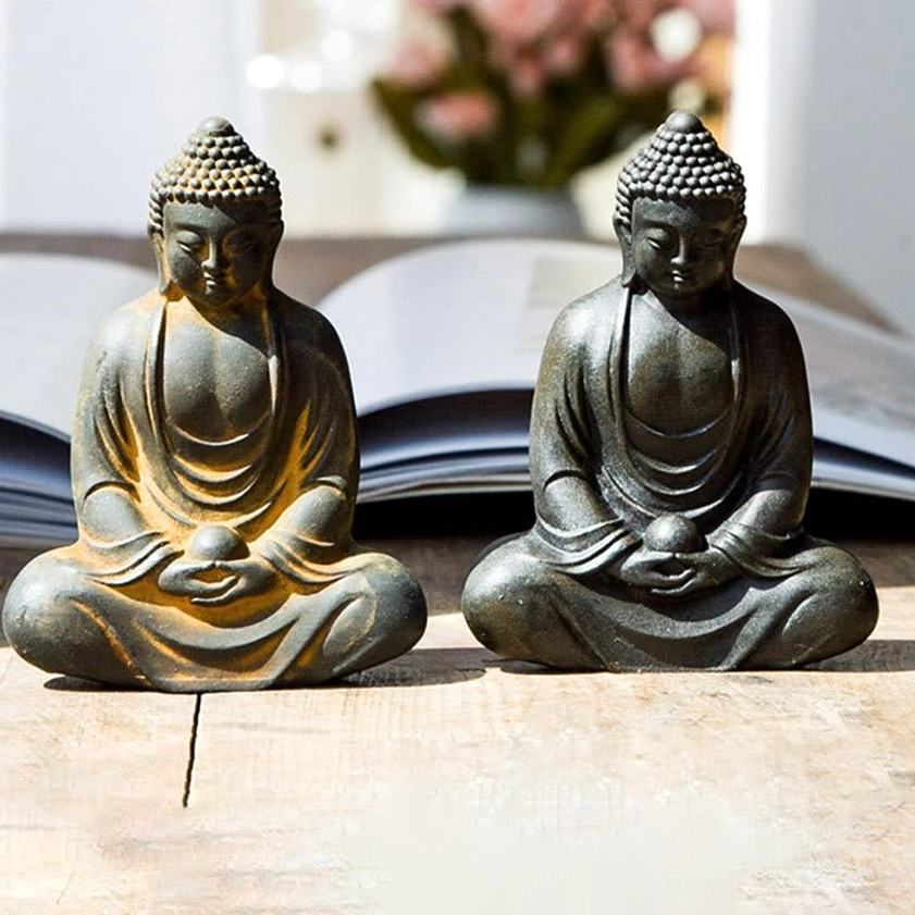Two matching meditating Buddha statues displayed together on wooden table with open book, dark grey with rustic yellow trim