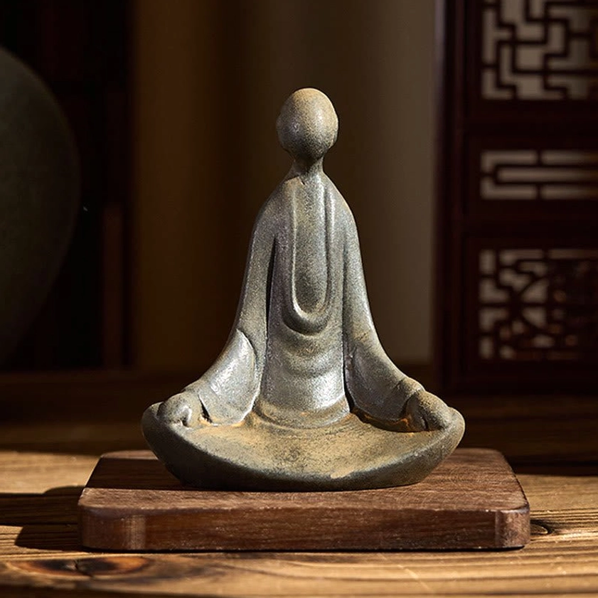 Faceless Buddha sitting statue with aged patina on wooden desk with lattice backdrop and square coaster