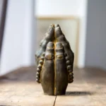 Handcrafted Buddha Namaste hand statue with aged rust bronze finish and prayer beads, displayed on wooden table with spiritual calm atmosphere