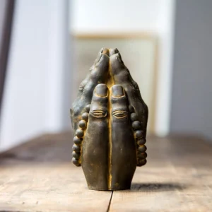 Handcrafted Buddha Namaste hand statue with aged rust bronze finish and prayer beads, displayed on wooden table with spiritual calm atmosphere