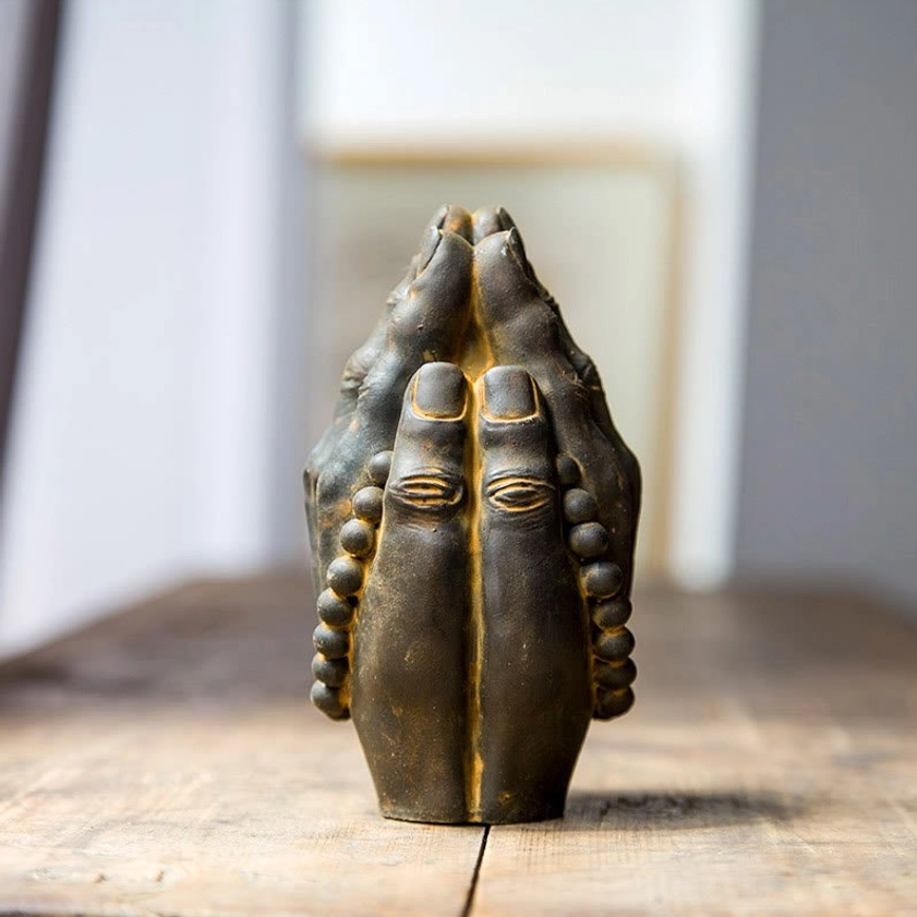Handcrafted Buddha Namaste hand statue with aged rust bronze finish and prayer beads, displayed on wooden table with spiritual calm atmosphere