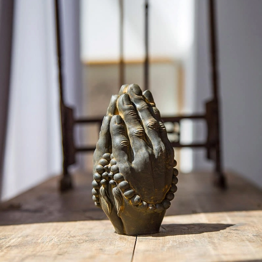 Buddha Namaste hand decoration with aged rust bronze patina and prayer beads, low-angle frontal view with traditional wooden furniture