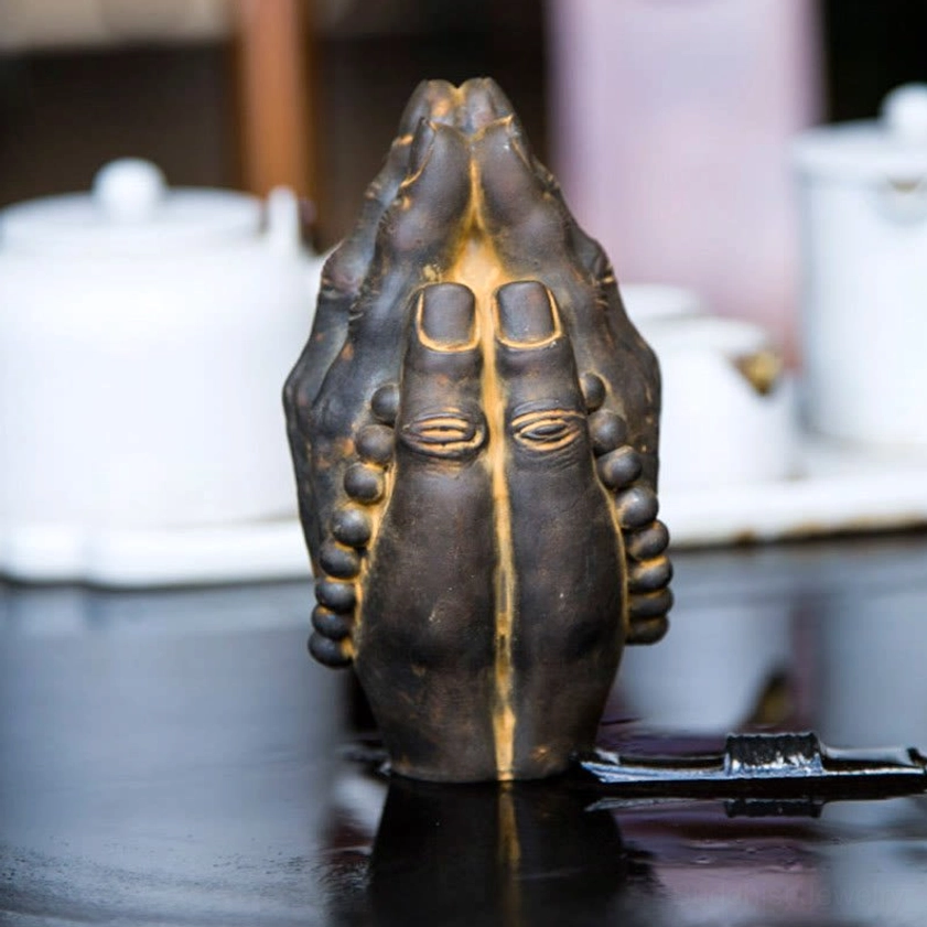 Iron powder resin Buddha hand ornament rear view with dark bronze color and yellow embossed palm eye details on ceramic background