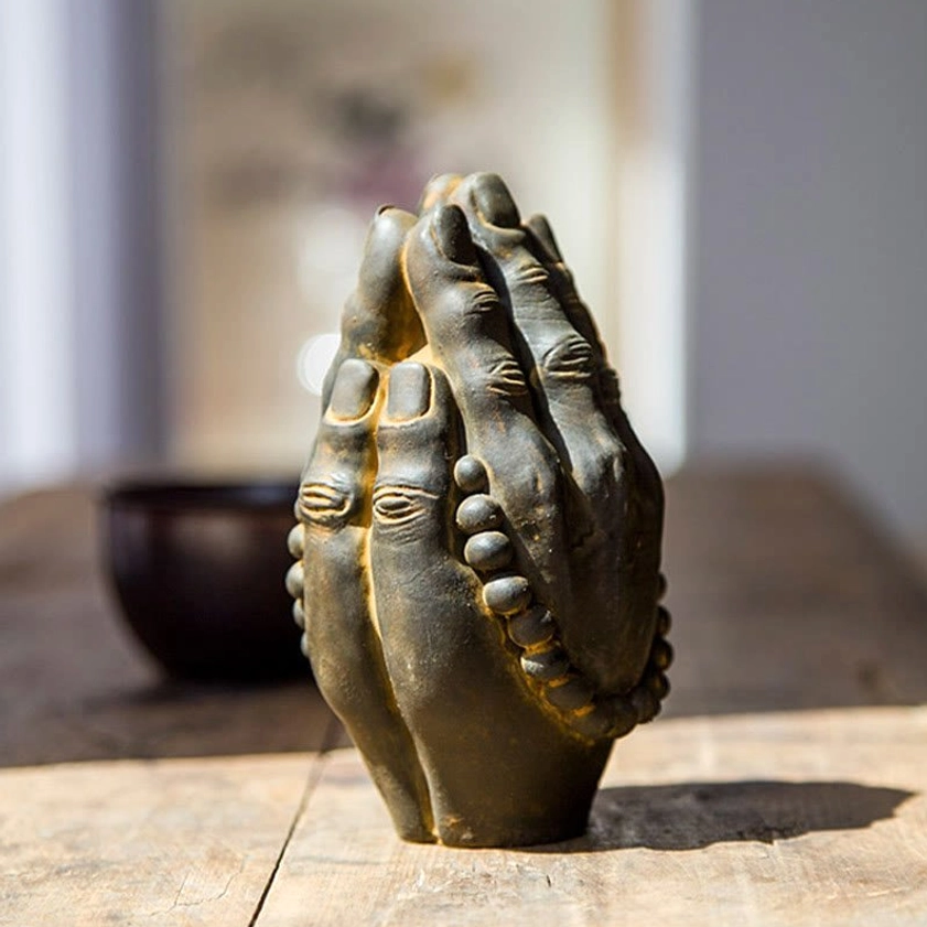 Iron powder resin Buddha Namaste hand ornament with dark bronze patina and yellow worn edges, three-quarter angle view with ceramic bowl