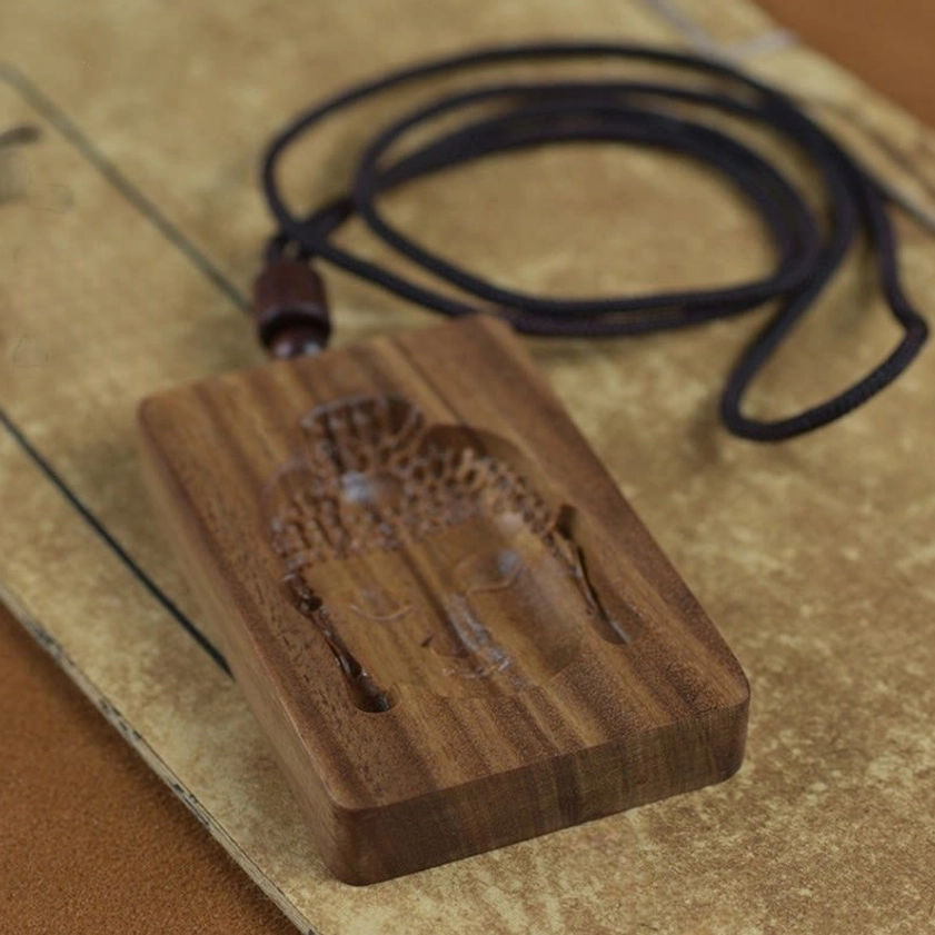 Top view of reverse side green sandalwood Buddha pendant necklace with coiled black rope cord on vintage paper background