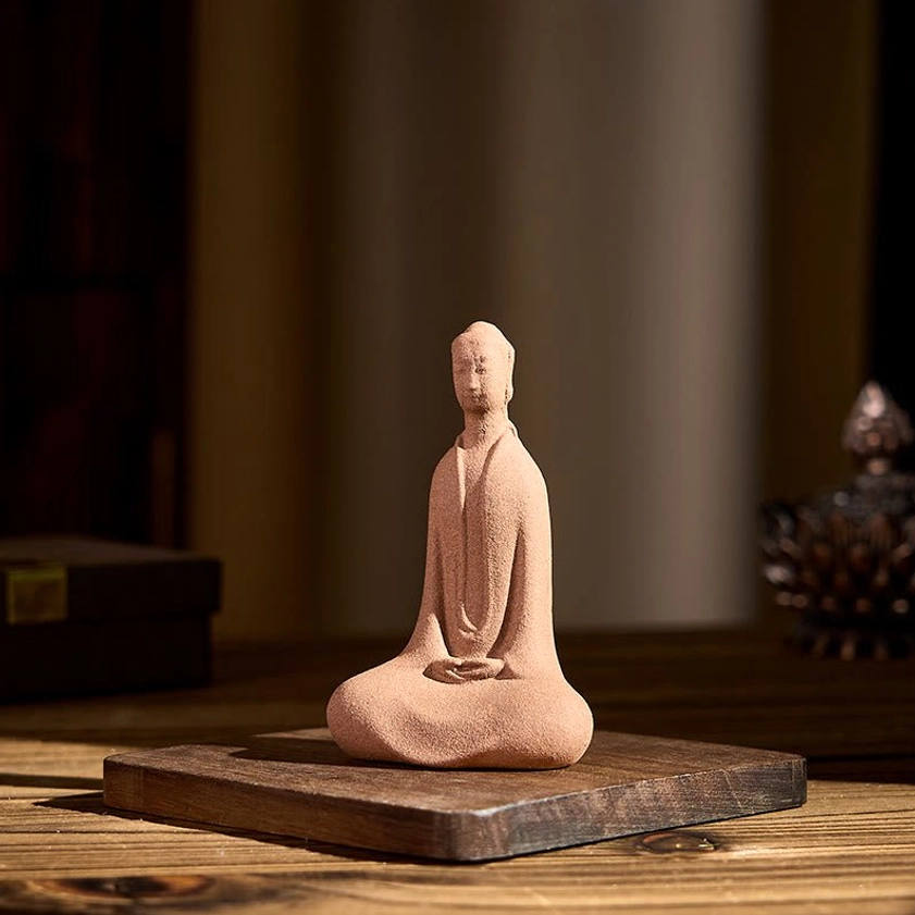 Seated Buddha ornament on wooden table with three-quarter front view, sand-textured matte ceramic surface with decorative props